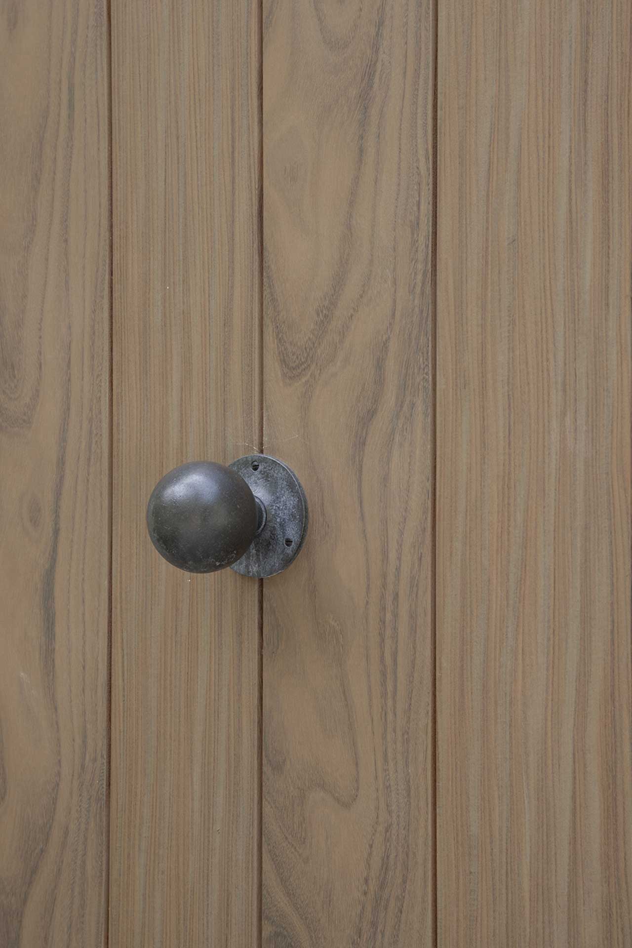 Detail einer modernen Haustür aus Holz mit vertikalen Paneelen und rundem, dunklen Türknauf.