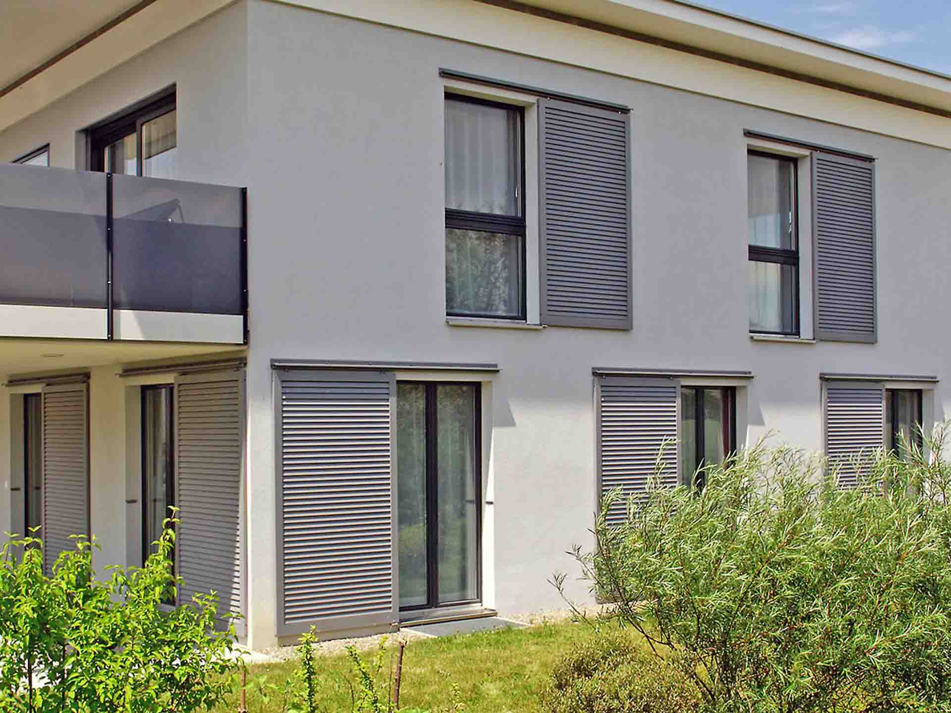 Modernes Wohnhaus mit Fenstern und Terrassentür, ausgestattet mit grauen Raffstores zum Sonnenschutz.