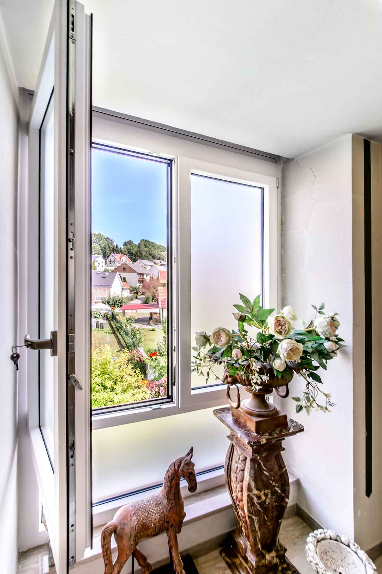 Geöffnetes, weißes Kunststoff-Aluminium-Fenster mit satiniertem Glas.