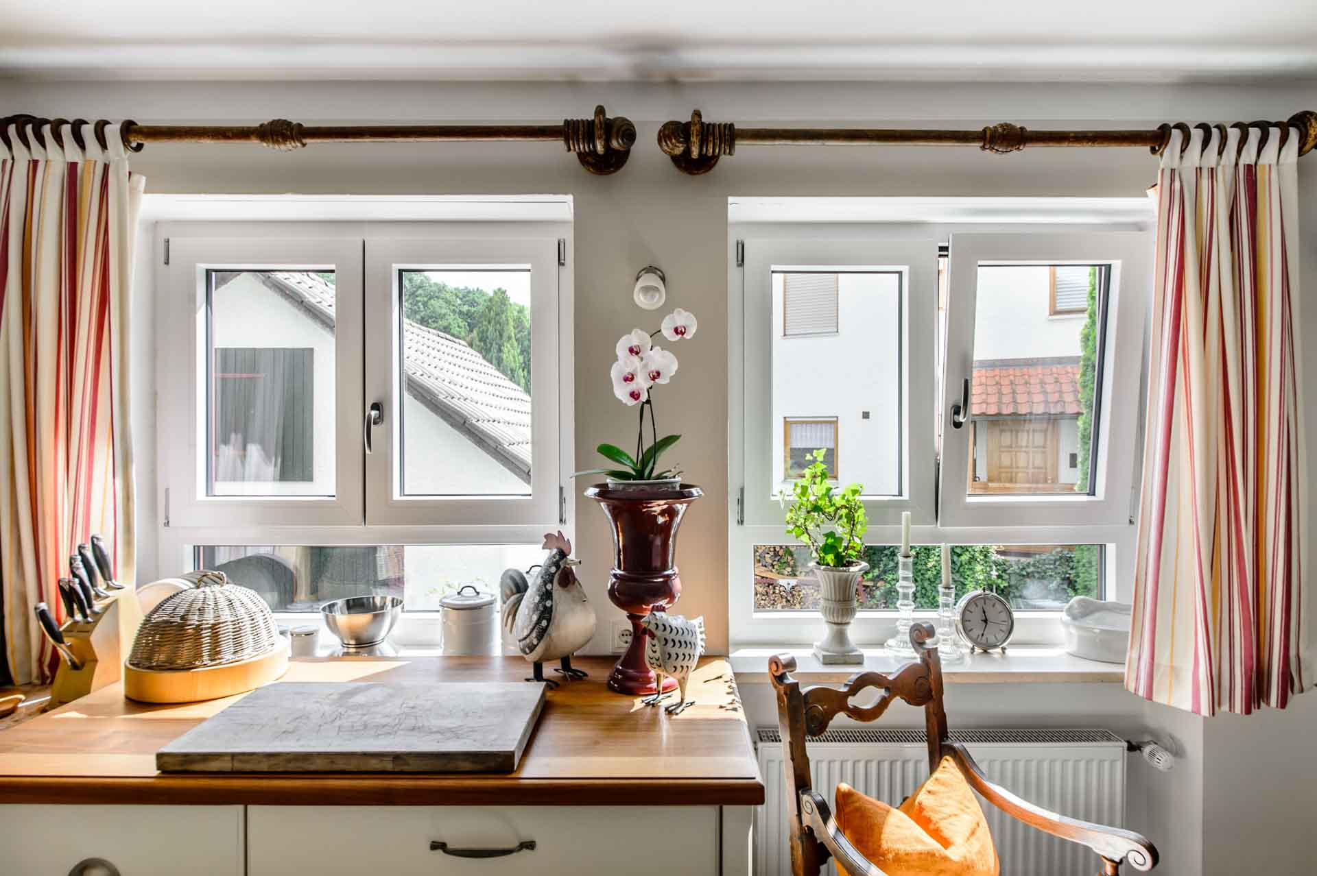 Zwei weiße Kunststoff-Aluminium-Fenster in der Küche mit Blumen und Hahn-Dekoration.
