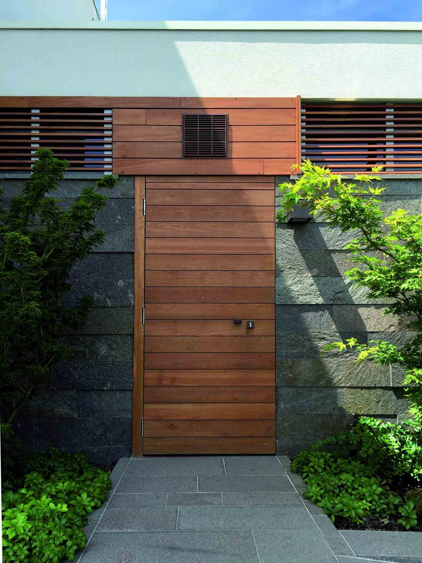 Flächenbündige Haustür aus dunklem Holz mit horizontaler Verlattung in moderner Fassade.
