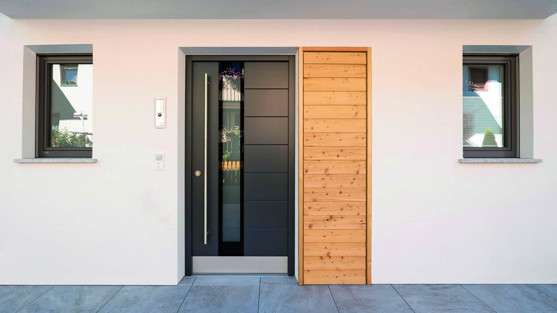 Breite Haustür in Grau mit Seitenteil und langer Edelstahlgriffstange.