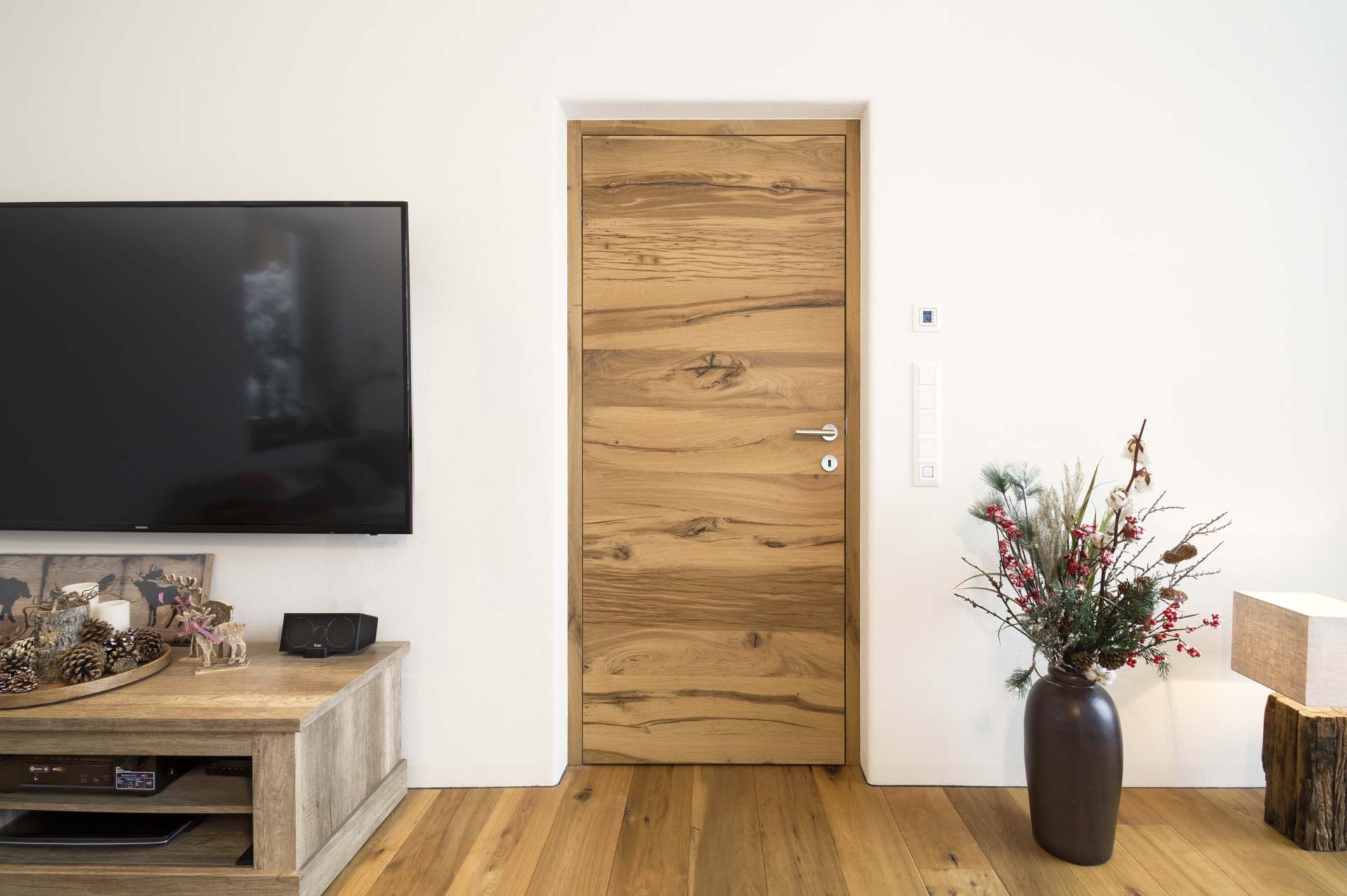 Massivholz-Wohnungseingangstür aus Eiche mit markanter Maserung, rahmenlos in weißer Wand integriert.