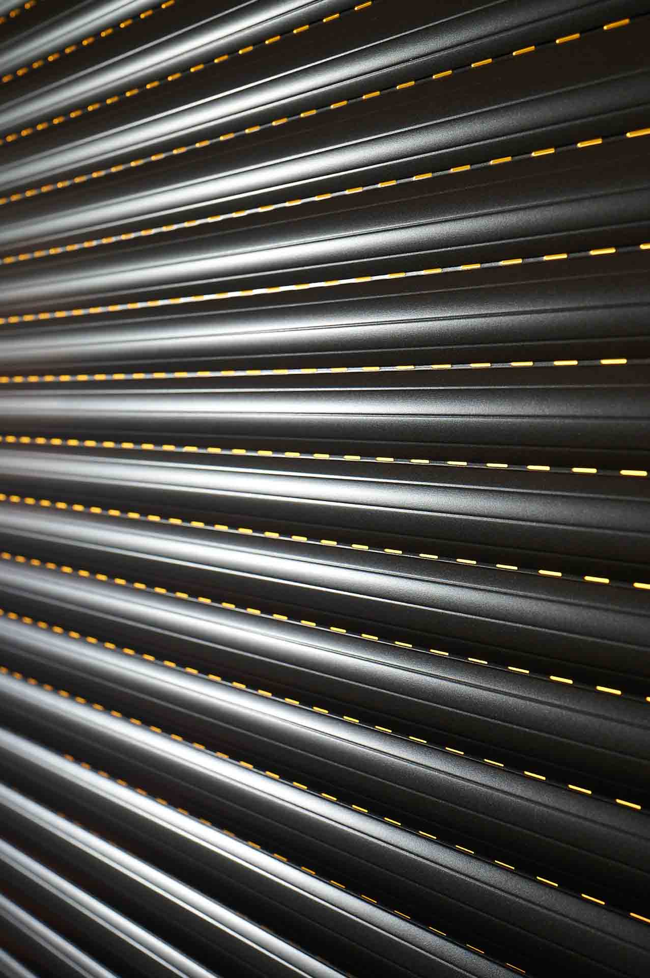 Nahaufnahme eines geschlossenen, dunklen Rollladens mit feinen Lichtschlitzen.