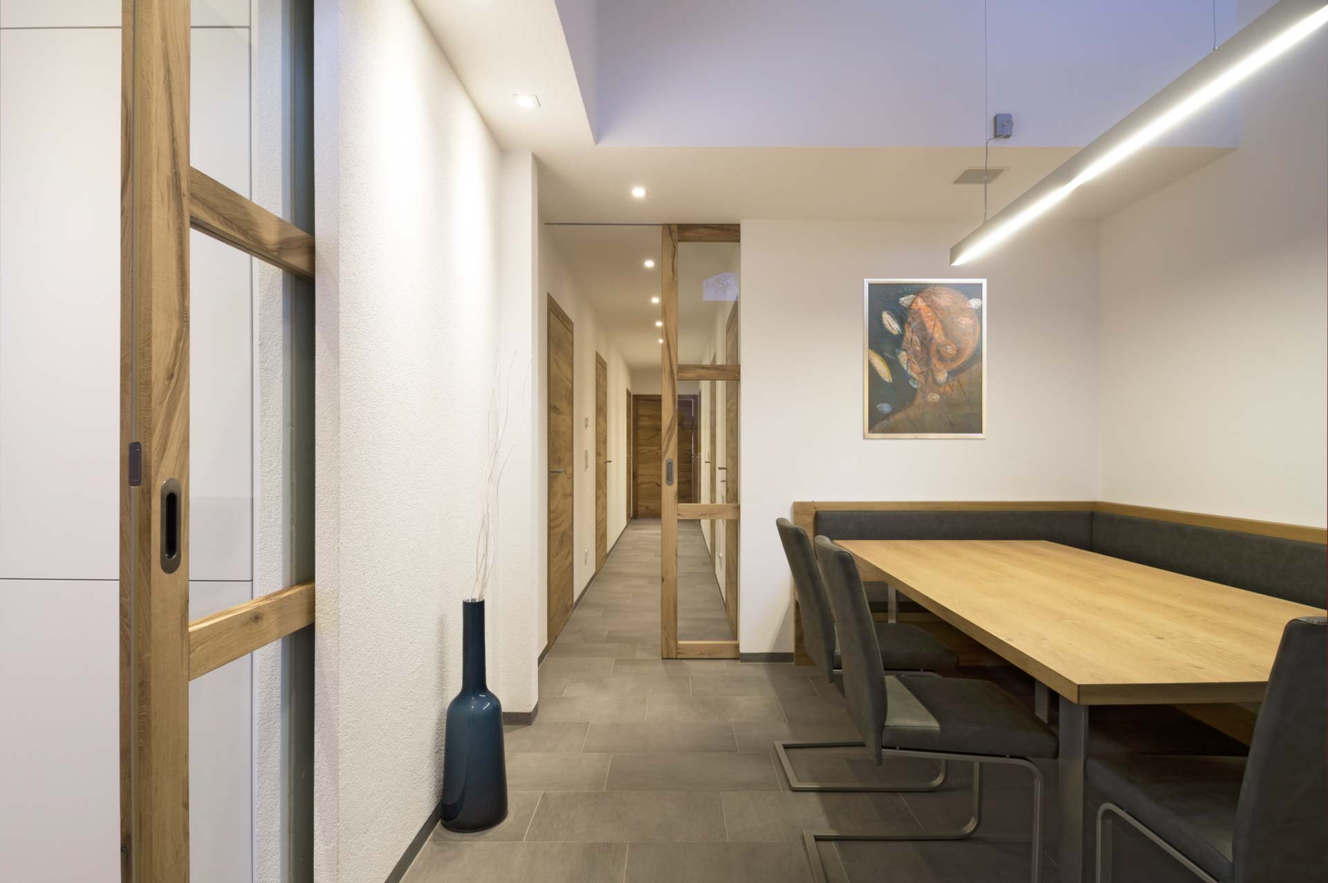 Offene Schiebetür aus Eichenholz und eine Glas-Schiebetür im Hintergrund in einem modernen Ess- und Flurbereich.